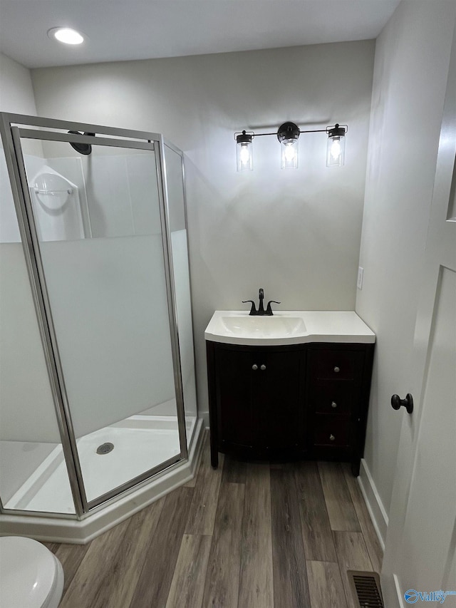 bathroom with toilet, vanity, hardwood / wood-style floors, and an enclosed shower