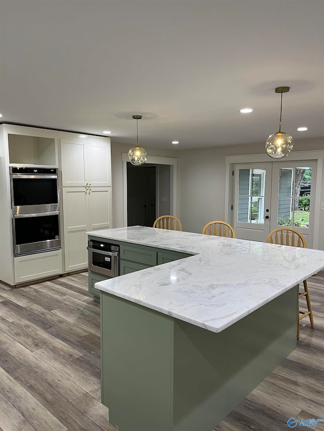 kitchen featuring stainless steel double oven, decorative light fixtures, light wood-type flooring, and white cabinetry