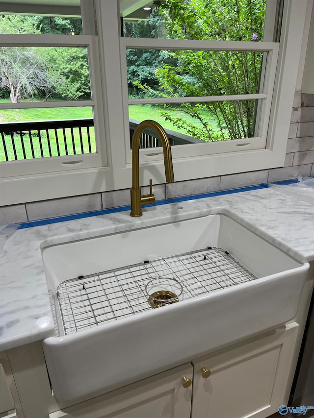 details featuring white cabinets, sink, light stone counters, and tasteful backsplash