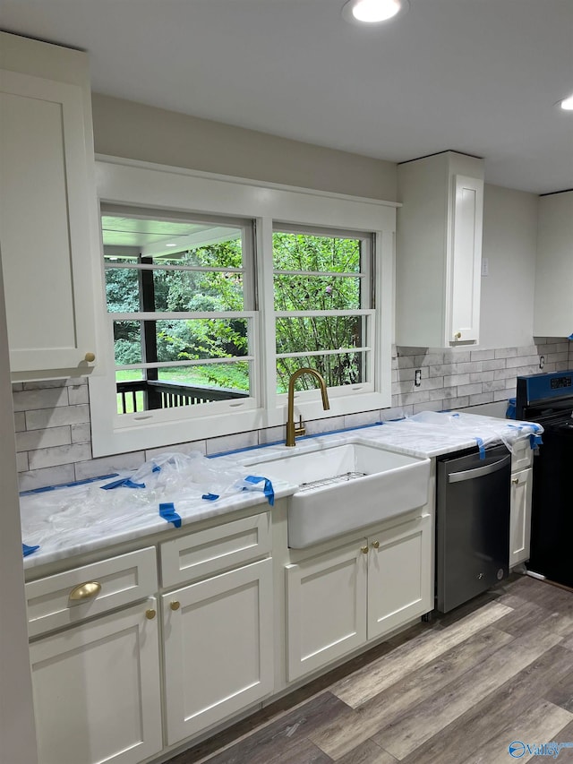 kitchen with decorative backsplash, light hardwood / wood-style floors, white cabinetry, light stone countertops, and stainless steel dishwasher