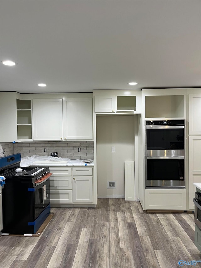 kitchen featuring white cabinets, backsplash, double oven, black stove, and hardwood / wood-style floors