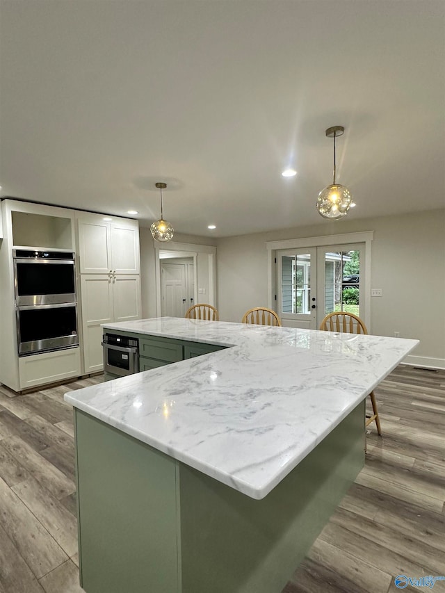 kitchen with pendant lighting, white cabinets, light hardwood / wood-style floors, and double oven