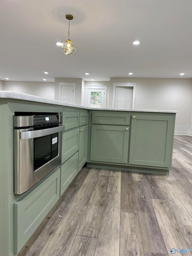 kitchen with oven, green cabinetry, hardwood / wood-style floors, and decorative light fixtures