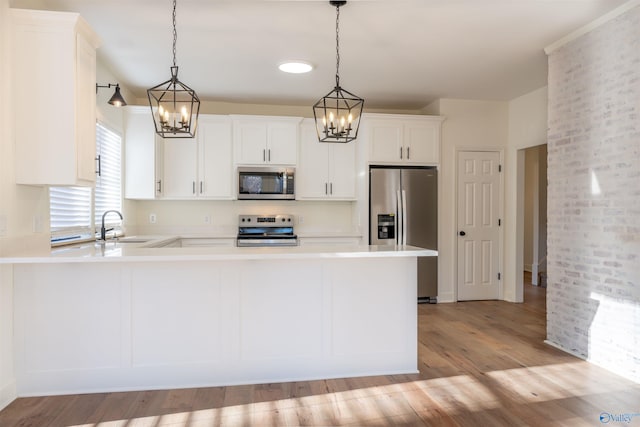 kitchen with a peninsula, stainless steel appliances, light countertops, light wood-type flooring, and a sink