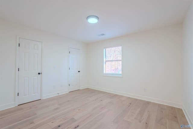 unfurnished room with light wood-type flooring, visible vents, and baseboards