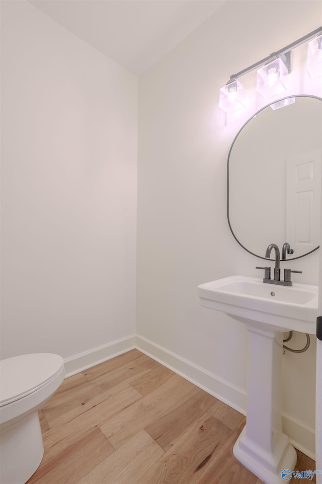 bathroom with toilet, baseboards, and wood finished floors