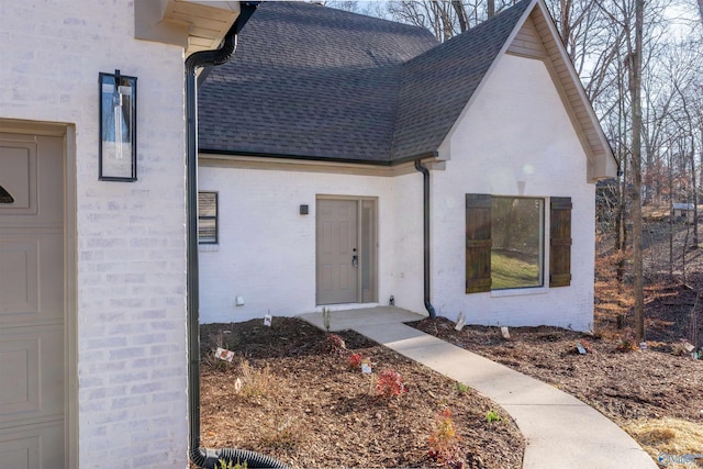 doorway to property with a garage, roof with shingles, and brick siding