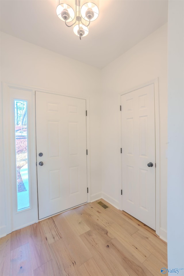 foyer entrance with baseboards, light wood finished floors, visible vents, and an inviting chandelier