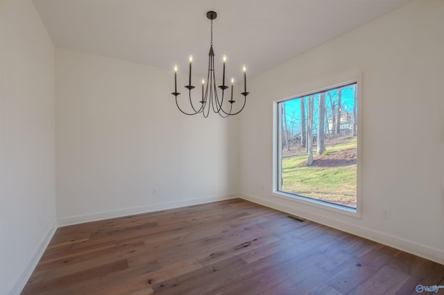 unfurnished dining area with visible vents, a notable chandelier, baseboards, and wood finished floors