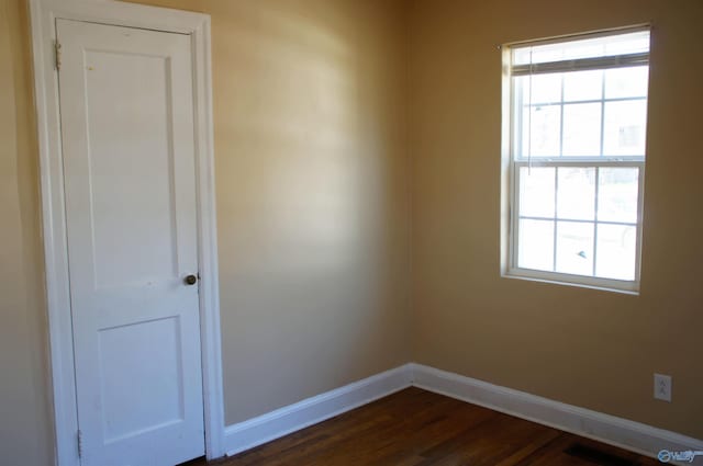 empty room with dark wood-type flooring, visible vents, and baseboards