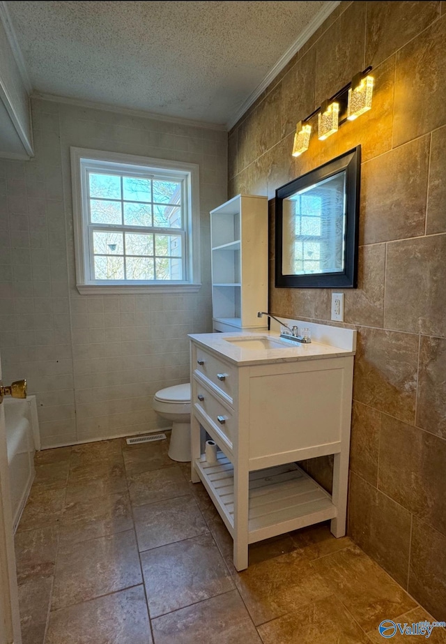 bathroom with toilet, a textured ceiling, tile walls, crown molding, and vanity