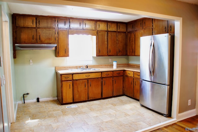kitchen with a sink, visible vents, brown cabinetry, and freestanding refrigerator