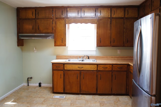 kitchen with brown cabinetry, freestanding refrigerator, a sink, light countertops, and under cabinet range hood