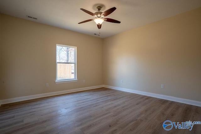 unfurnished room with dark wood-style floors, visible vents, a ceiling fan, and baseboards