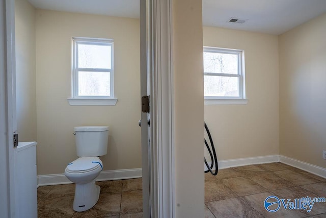 bathroom with toilet, visible vents, plenty of natural light, and baseboards