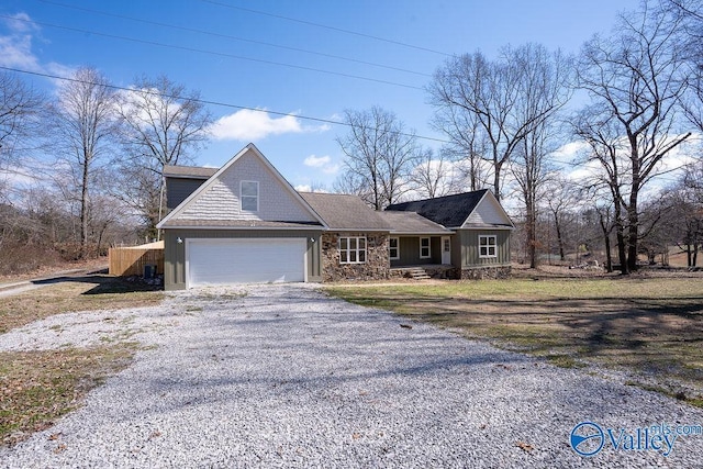 view of front of property featuring a garage, gravel driveway, and stone siding