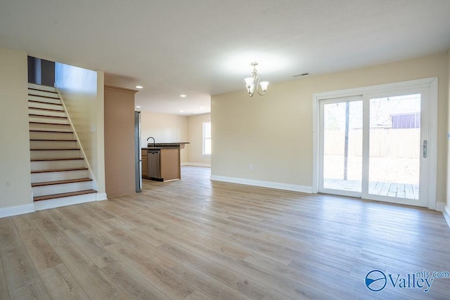 unfurnished living room featuring visible vents, baseboards, light wood-style flooring, stairway, and a chandelier