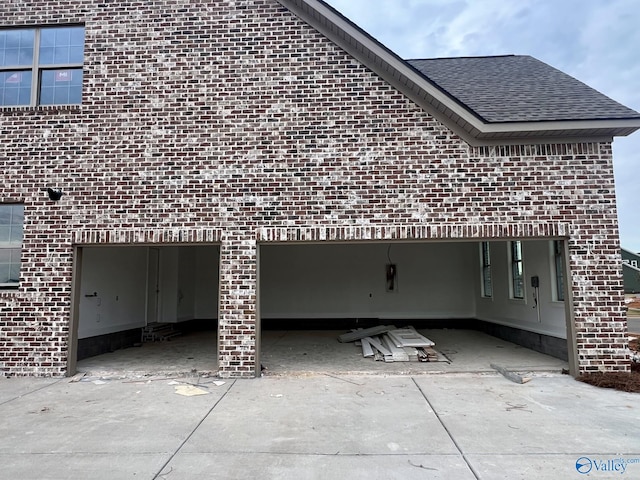 view of side of home with a garage, brick siding, concrete driveway, and roof with shingles