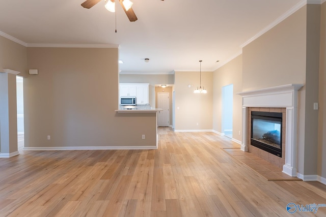 unfurnished living room with ceiling fan with notable chandelier, a fireplace, ornamental molding, and light hardwood / wood-style flooring