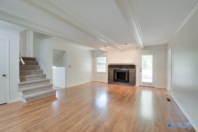 unfurnished living room with ornamental molding, beam ceiling, light hardwood / wood-style flooring, and a tiled fireplace