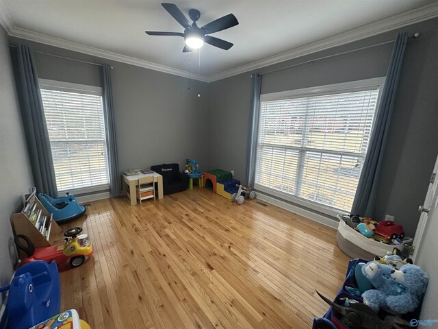 recreation room with wood-type flooring, ceiling fan, and crown molding