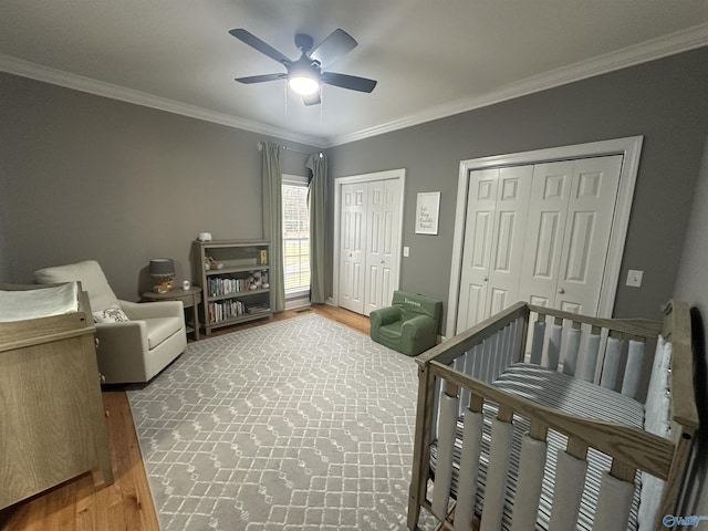 bedroom with hardwood / wood-style floors, ceiling fan, ornamental molding, and a nursery area