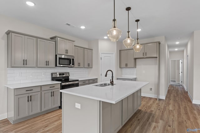 kitchen featuring appliances with stainless steel finishes, pendant lighting, gray cabinets, light wood-type flooring, and sink