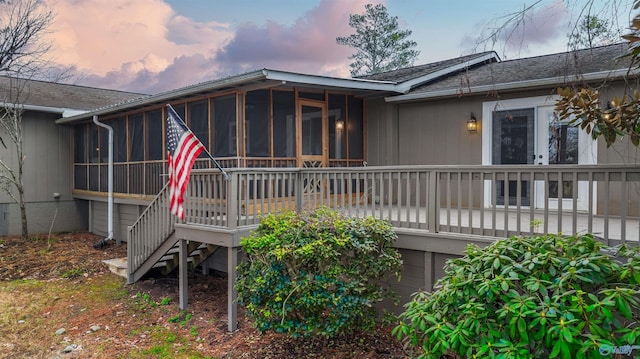 back house at dusk featuring a sunroom and a deck