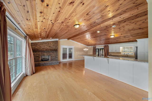 unfurnished living room with lofted ceiling, sink, a stone fireplace, and light wood-type flooring