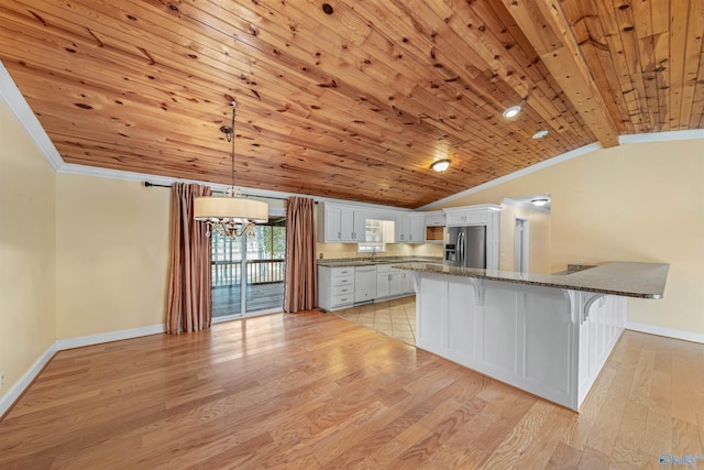 kitchen featuring white cabinets, stainless steel fridge, a kitchen bar, hanging light fixtures, and crown molding