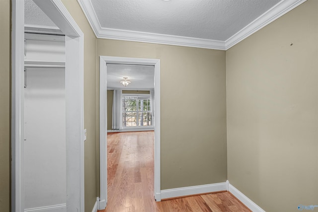 hallway featuring ornamental molding, light hardwood / wood-style floors, and a textured ceiling