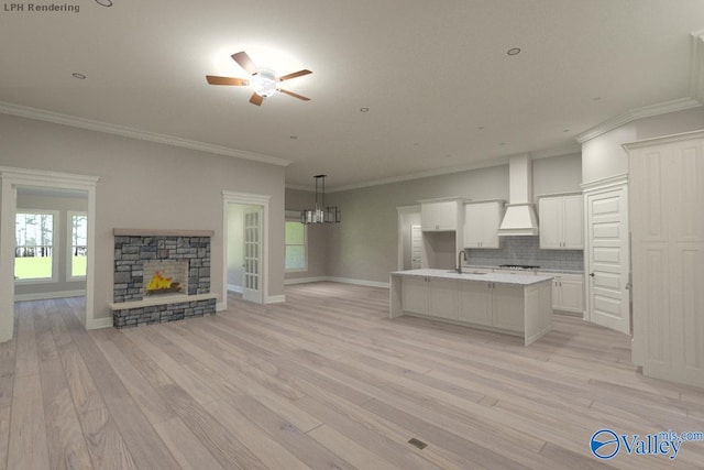 kitchen featuring an island with sink, decorative backsplash, crown molding, white cabinetry, and a fireplace