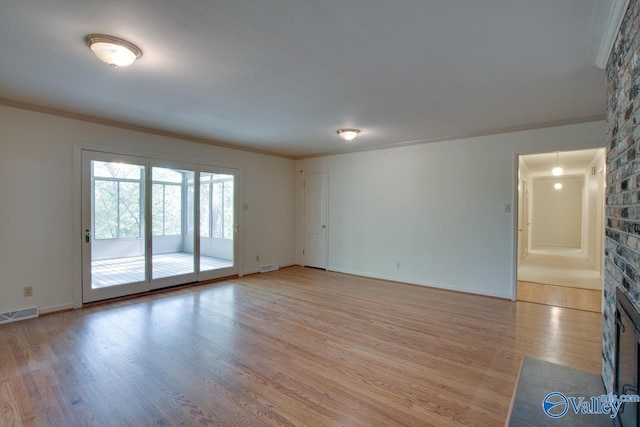 empty room featuring a brick fireplace, light hardwood / wood-style floors, and ornamental molding