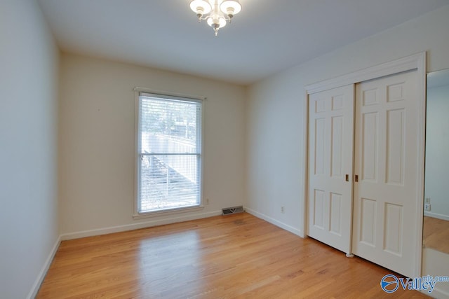 unfurnished bedroom featuring a closet, a notable chandelier, and light wood-type flooring