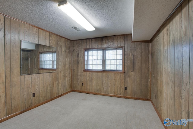 spare room featuring wood walls, light colored carpet, and a textured ceiling