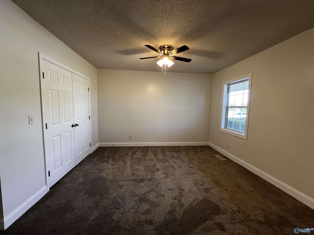 unfurnished bedroom featuring a textured ceiling, dark carpet, visible vents, and baseboards