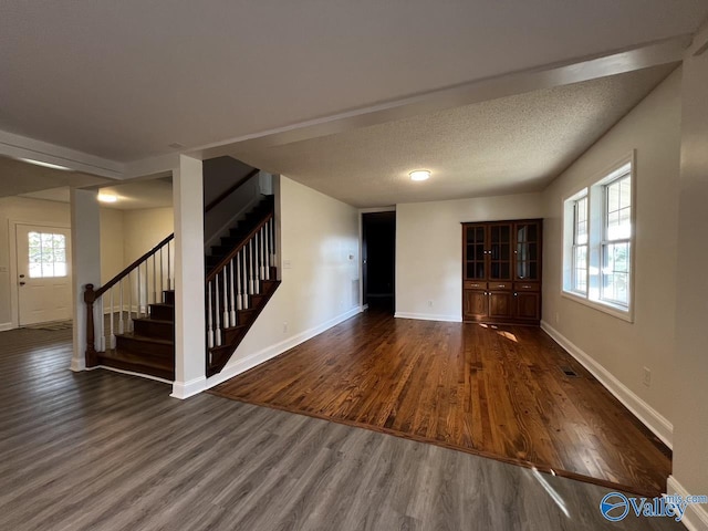 unfurnished living room featuring a textured ceiling, stairs, baseboards, and dark wood-style flooring