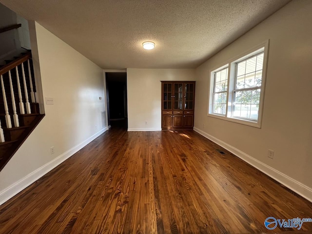 unfurnished living room with a textured ceiling, dark wood-style flooring, visible vents, baseboards, and stairway