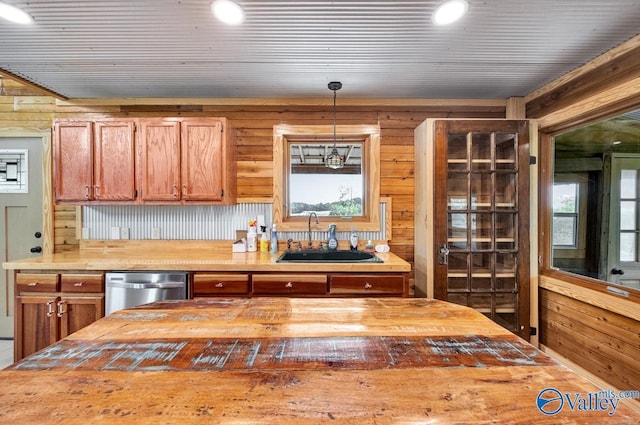 kitchen featuring butcher block countertops, wood walls, sink, hanging light fixtures, and stainless steel dishwasher