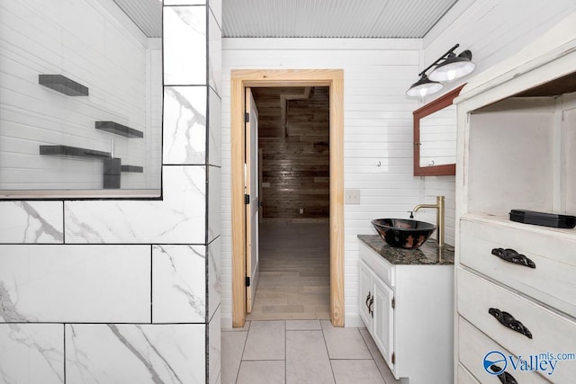 kitchen with sink, wood walls, light tile patterned floors, dark stone countertops, and white cabinets