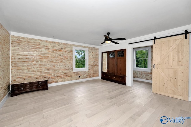 unfurnished living room with a barn door, brick wall, plenty of natural light, and light wood-type flooring