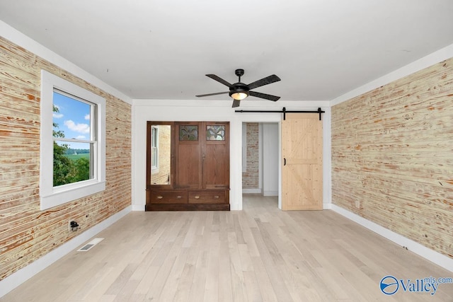 unfurnished bedroom featuring brick wall, ceiling fan, a barn door, and light hardwood / wood-style floors