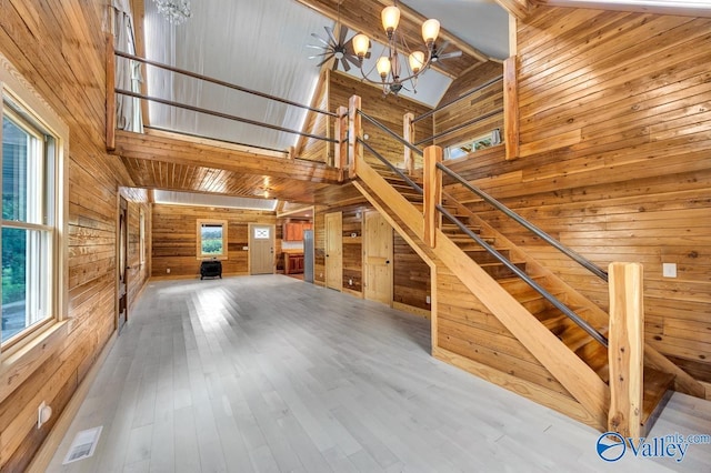 unfurnished living room with a notable chandelier, wood-type flooring, high vaulted ceiling, and wood walls