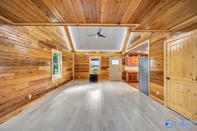 unfurnished living room featuring wood ceiling, light hardwood / wood-style flooring, a wood stove, ceiling fan, and wood walls