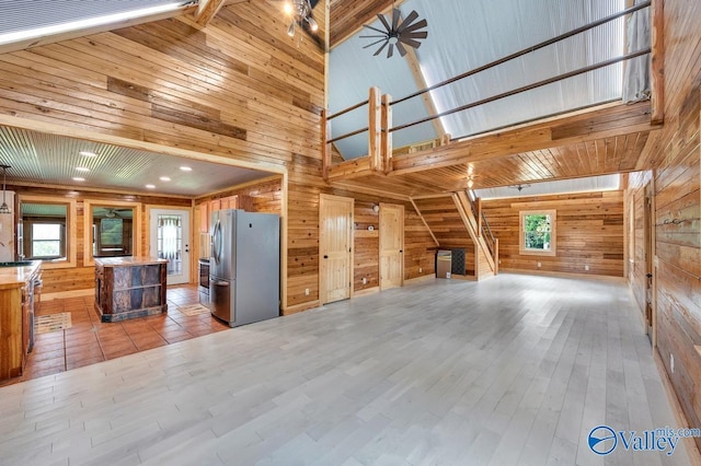 unfurnished living room featuring a towering ceiling, light hardwood / wood-style floors, and wood walls