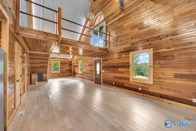 unfurnished living room with light hardwood / wood-style flooring, a towering ceiling, and wooden walls