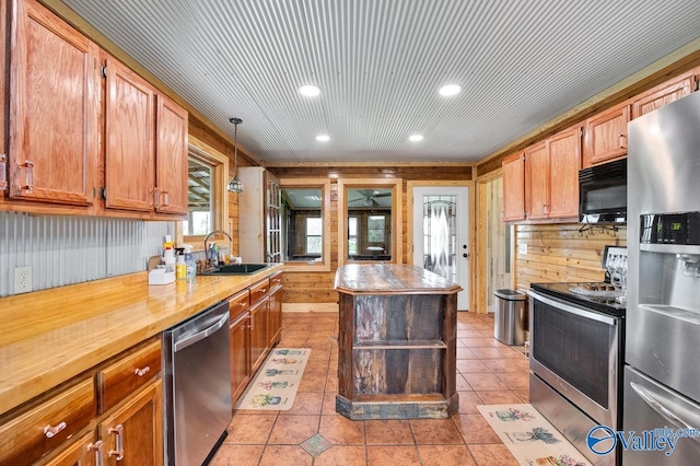 kitchen with sink, light tile patterned floors, stainless steel appliances, decorative light fixtures, and wood walls