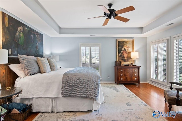 bedroom with hardwood / wood-style flooring, ceiling fan, and a tray ceiling