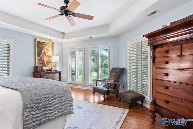 bedroom with hardwood / wood-style flooring, ceiling fan, and a tray ceiling