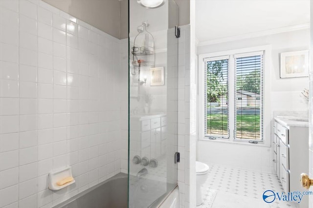 full bathroom featuring crown molding, combined bath / shower with glass door, tile walls, vanity, and toilet